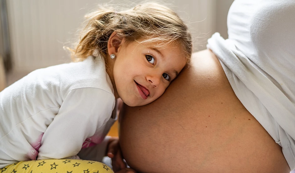 Mädchen legt den Kopf auf den Bauch der schwangeren Mutter.