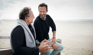 Zwei Männer sitzen am Strand und unterhalten sich.