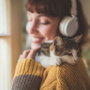 Frau zu Hause hört Musik und kuschelt mit ihrer Katze