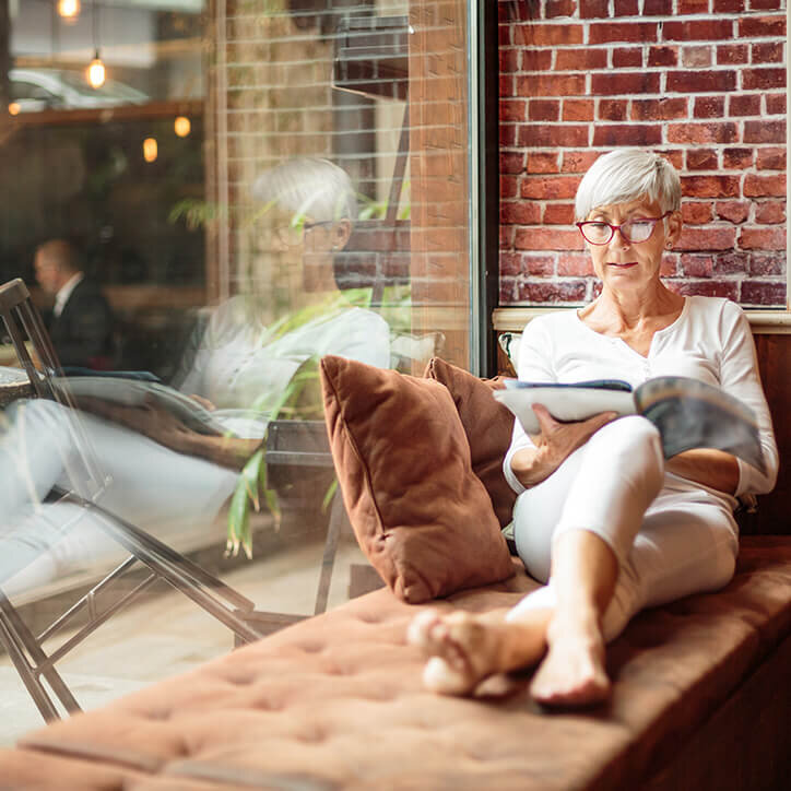 Ältere Frau liest ein Magazin am Fenster in einem Café | Doppelherz