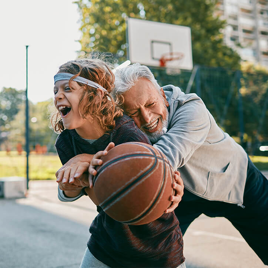 Älterer Mann umarmt lachend Jungen mit Basketball