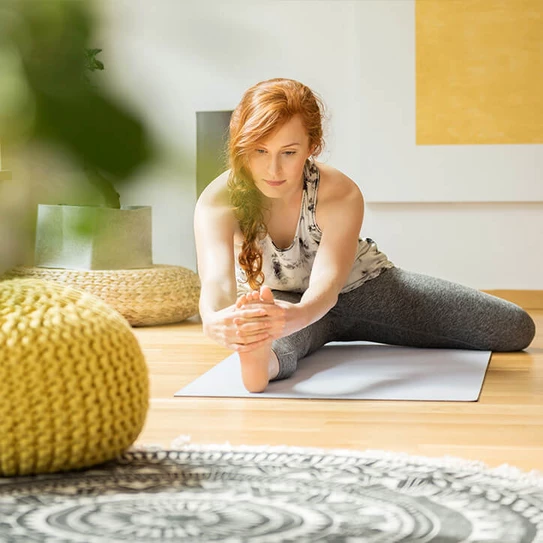 Junge Frau dehnt sich zu Hause auf einer Yogamatte