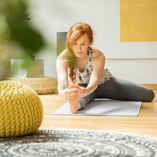 Junge Frau dehnt sich zu Hause auf einer Yogamatte