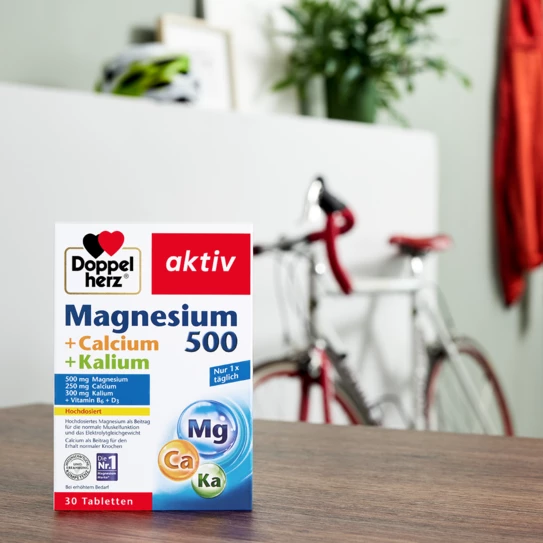 Doppelherz Magnesium 500 + Calcium + Kalium auf Tisch mit Fahrrad im Hintergrund