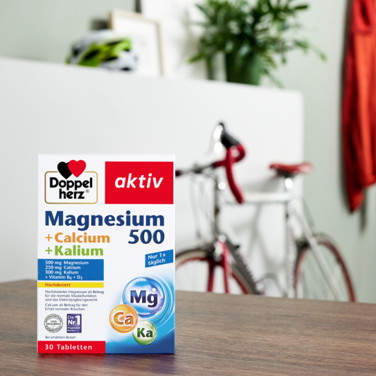 Doppelherz Magnesium 500 + Calcium + Kalium auf Tisch mit Fahrrad im Hintergrund
