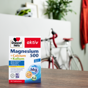 Doppelherz Magnesium 500 + Calcium + Kalium auf Tisch mit Fahrrad im Hintergrund