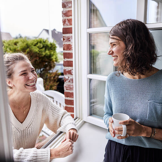 Zwei glückliche Frauen unterhalten sich durch Fenster