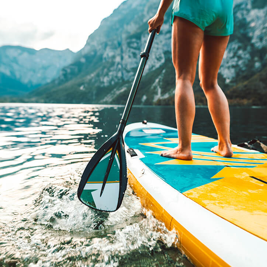 Frau paddelt auf Paddleboard auf einem See umgeben von Bergen