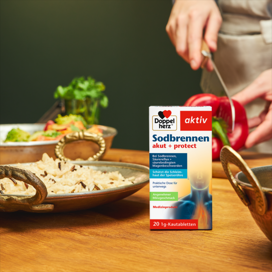 Doppelherz Sodbrennen akut + protect auf Küchentisch, Frau schneidet Paprika im Hintergrund