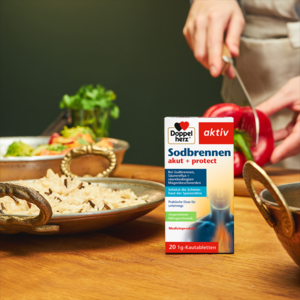 Doppelherz Sodbrennen akut + protect auf Küchentisch, Frau schneidet Paprika im Hintergrund