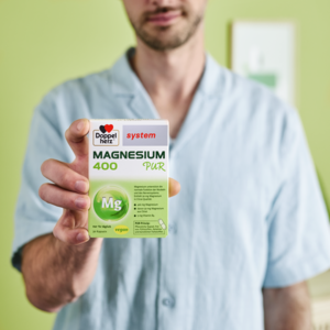 Mann hält Doppelherz system Magnesium 400 Pur in die Kamera