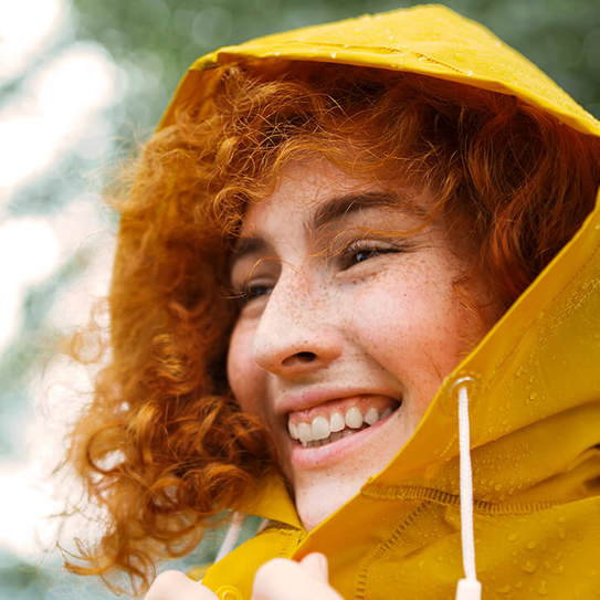 Portrait einer jungen Frau im gelben Regenmantel im Wald