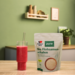 Doppelherz pure Bio Flohsamenschalen neben rotem Smoothie auf Tisch