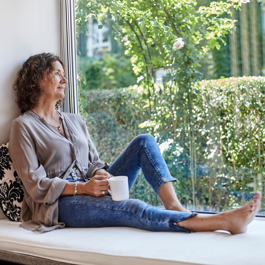 Frau sitzt mit Kaffeebecher auf Fensterbank