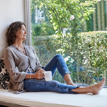 Frau sitzt mit Kaffeebecher auf Fensterbank