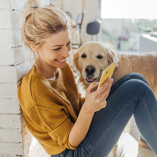 Foto einer jungen Frau, die Morgennachrichten online liest, während ihr Hund neben ihr steht