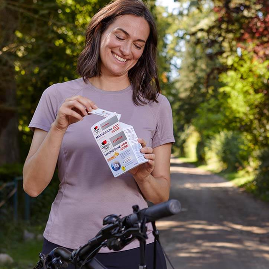 Frau auf Fahrrad holt Doppelherz system Magnesium 400 Direct aus der Packung