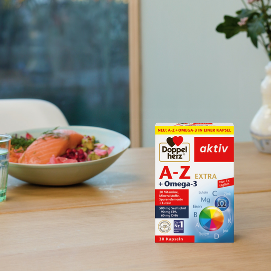 Doppelherz A-Z + Omega-3 auf Esstisch, Salat mit Lachs im Hintergrund