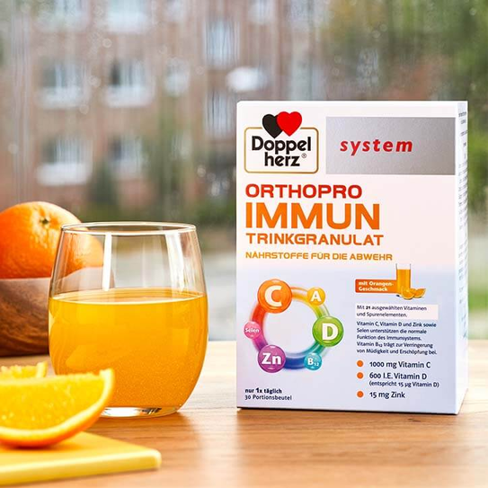 Doppelherz system Orthopro Immun auf Tisch neben Glas mit Orangensaft und Orangen