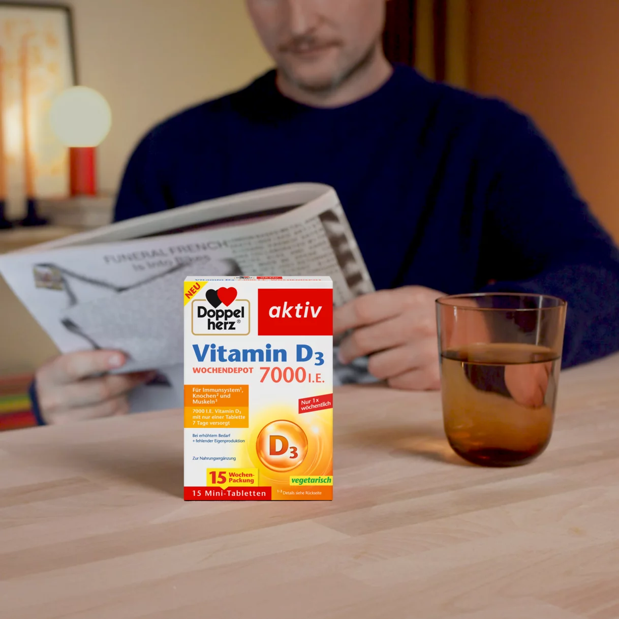 Doppelherz Vitamin D3 7000 I.E. auf Tisch mit Wasserglas, Mann mit Zeitung im Hintergrund
