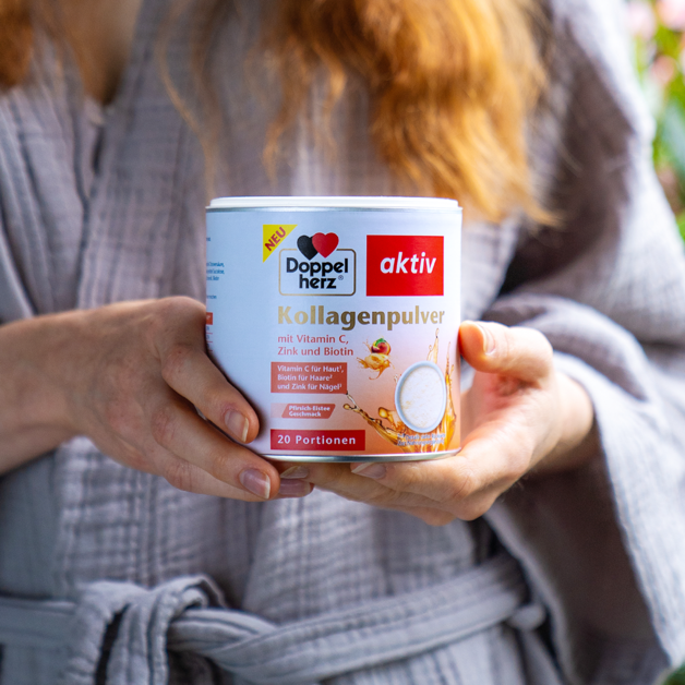 Eine Frau hält das Produkt Doppelherz Kollagenpulver Pfirsich-Eistee in ihren Händen.