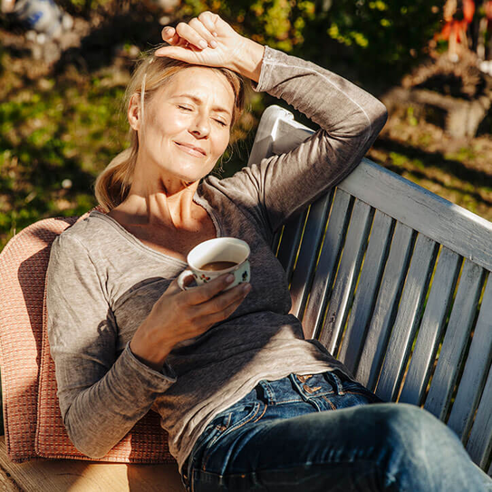 Frau entspannt mit Tasse Kaffee auf Gartenbank