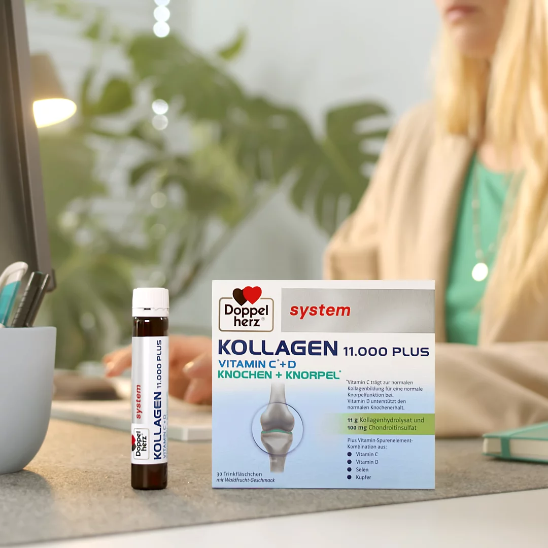 Doppelherz system Kollagen 11.000 Plus auf Schreibtisch neben arbeitender Frau
