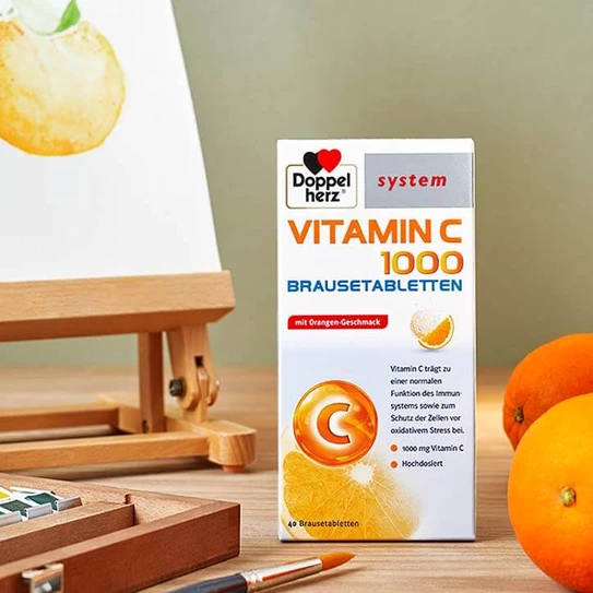 Doppelherz system Vitamin C 1000 Brausetabletten auf Tisch neben Staffelei und Orangen