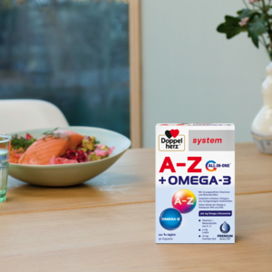 Doppelherz system A-Z + Omega-3 auf Esstisch, Salat mit Lachs im Hintergrund
