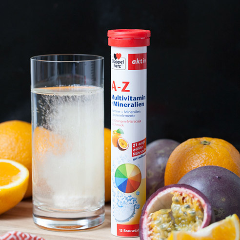 Doppelherz A-Z Brausetabletten, Brausetablette löst sich in Glas Wasser auf, daneben Orangen und Maracuja