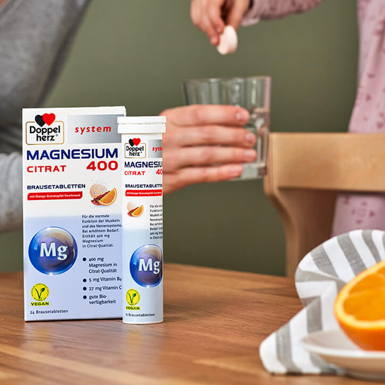 Doppelherz system Magnesium 400 Citrat Brausetabletten auf Tisch, Braustablette wird in Wasserglas geworfen