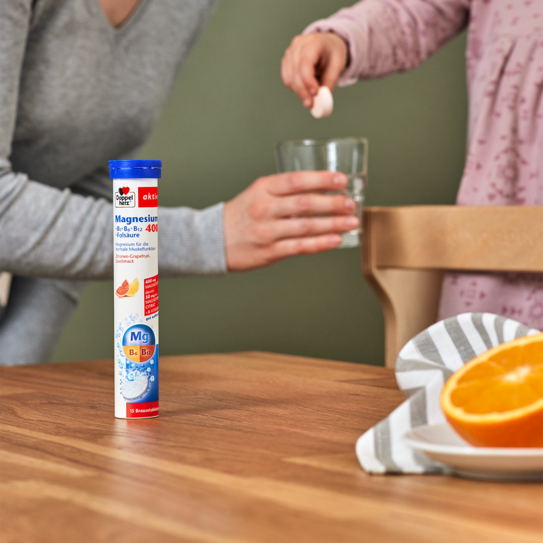 Doppelherz Magnesium 400 Brausetabletten auf Tisch, Brausetablette wird in Glas Wasser geworfen